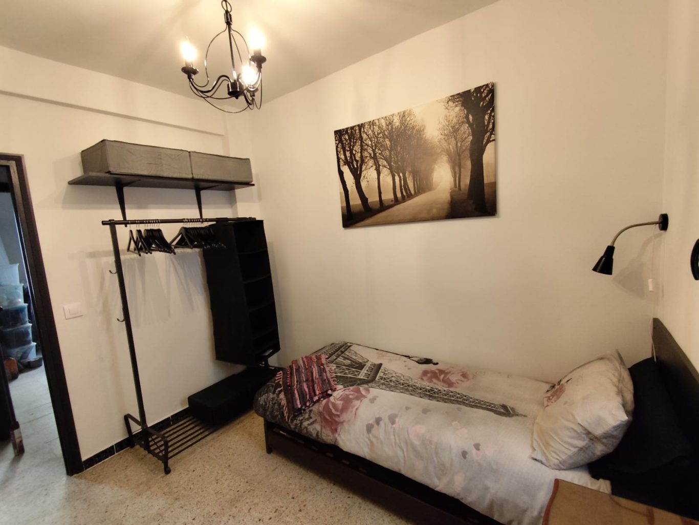 Habitación secundaria Habitación sencilla con cama, lámpara de pie y cuadro de un paisaje en la pared.